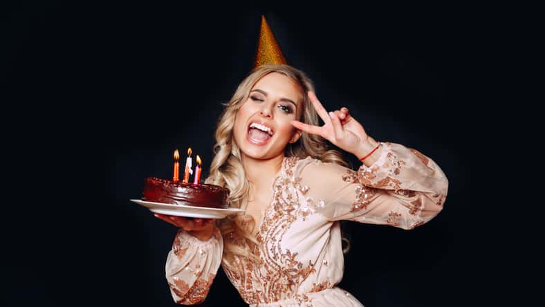 Portrait of a young beautiful blond girl holding birthday cake with candles and having fun