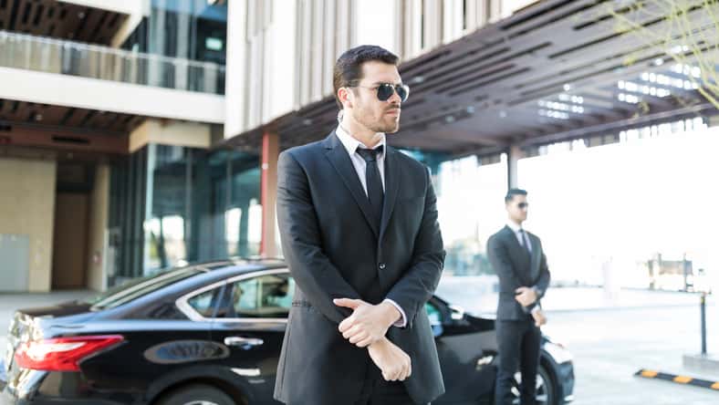 Alert bodyguard keeping an eye on surroundings with car parked on city street