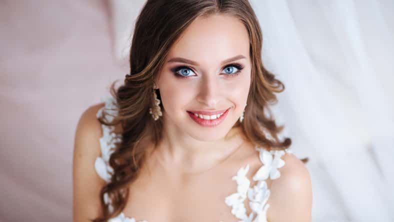 Beautiful bride with long hair in elegant wedding dress and diadem smiling in room in the wedding morning