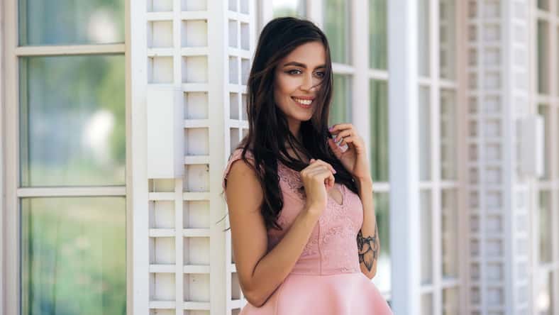 Cute model with beautiful smile in pink dress posing in street cafe.