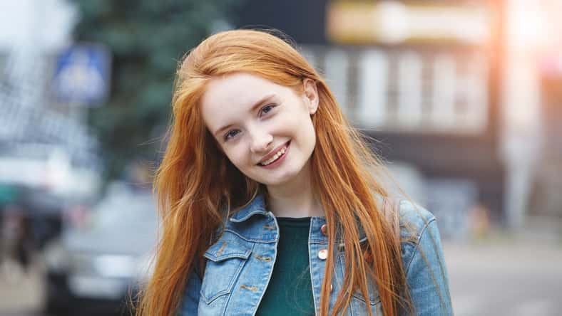 candid outdoor portrait of pretty smiling young girl with long red hair, morning sunrise light