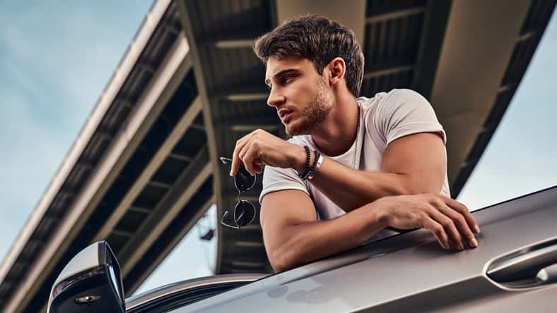 Handsome young man in casual clothes standing near his modern sport car on the street