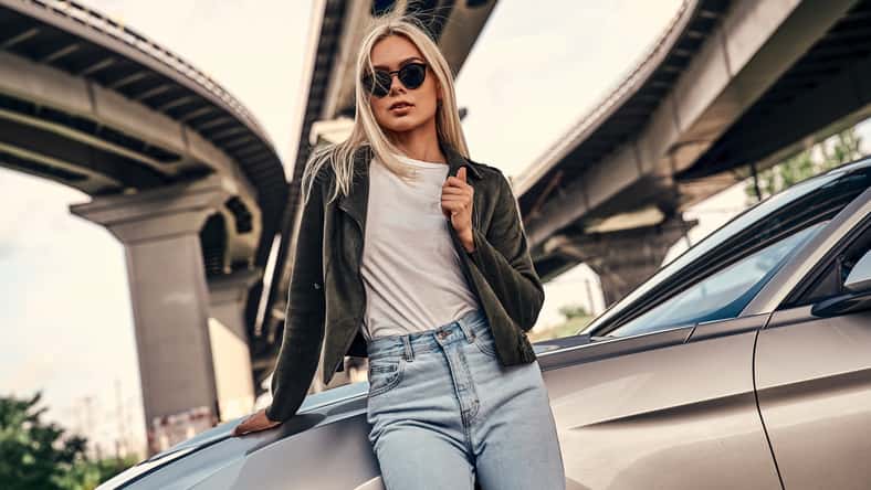 Attractive young blonde in casual clothes and sunglasses standing near sport car on the street. Urban style.