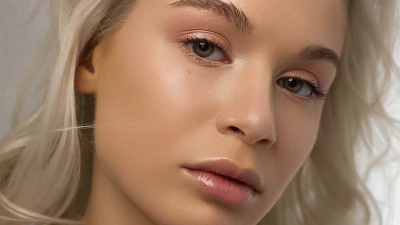 Closeup portrait of a woman with developing curly hair. Sweet tender young blonde girl. Natural lipstick, clear clear skin. Skin care with natural cosmetics in a spa or cosmetology.