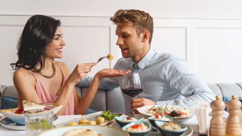 Beautiful young couple sitting at the table with delicious food and wine in restaurant