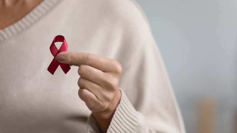 Close up of senior woman hold red ribbon breast cancer symbol support people patient with illness, middle-aged female volunteer keep AIDS HIV disease awareness, elderly healthcare, medicine concept