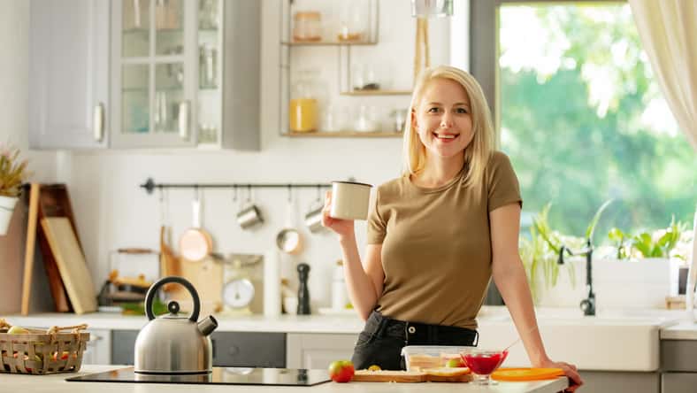blonde woman stands in the kitchen with a cup of coffee