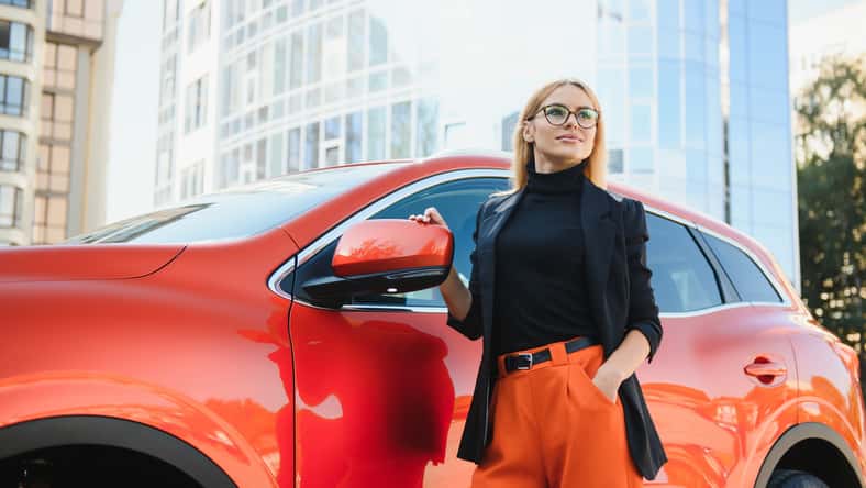 Yong pretty woman standing near a big all terrain car outdoors. Driver girl in casual clothes outside her vehicle.