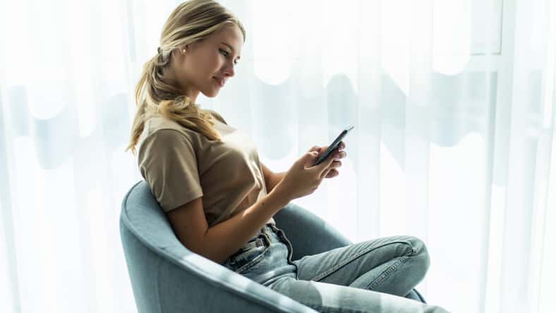 Beautiful woman sitting on a chair and texting a phone message
