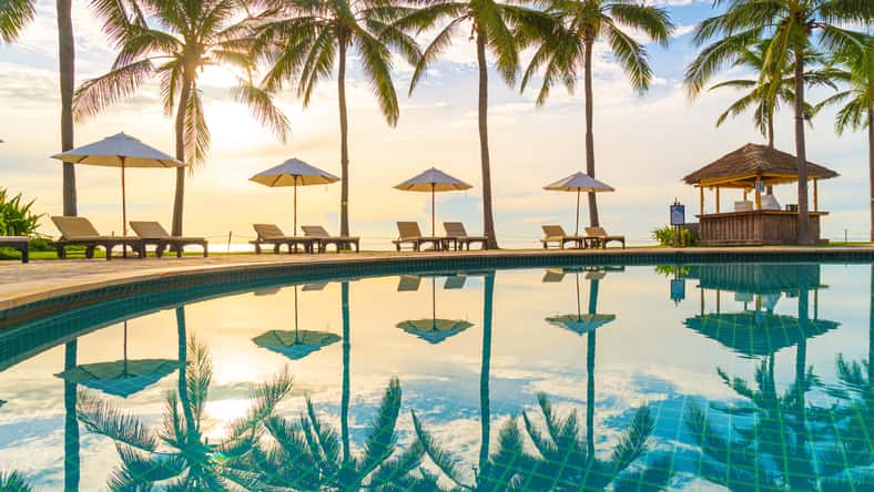 Beautiful luxury umbrella and chair around outdoor swimming pool in hotel and resort with coconut palm tree on sunset or sunrise sky - holiday and vacation concept