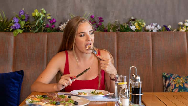Beautiful young woman in red dress eating alone in the restaurant