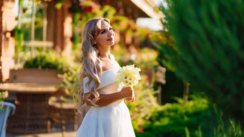 beautiful blonde bride with a bouquet of callas on the path in the garden. wedding in the park. the concept of choosing a place for the celebration.