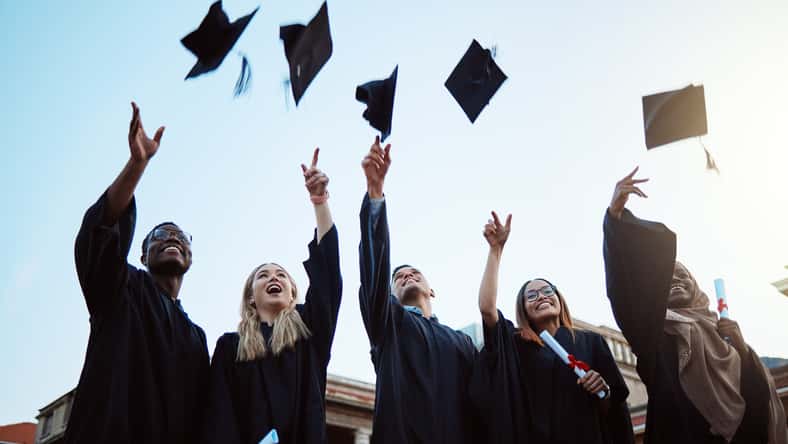 Graduation, education and success with friends in celebration as a graduate group outdoor, throwing mortar caps. Diversity, university and man and woman students celebrating a college diploma.