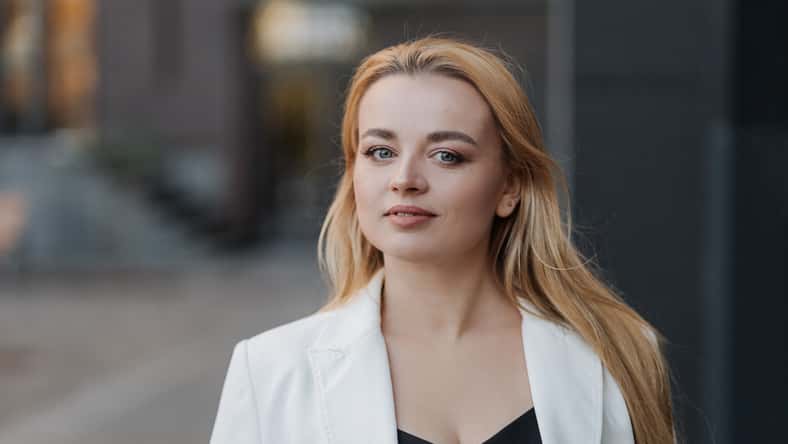Blond stylish woman at oversized white jacket posing on the city background