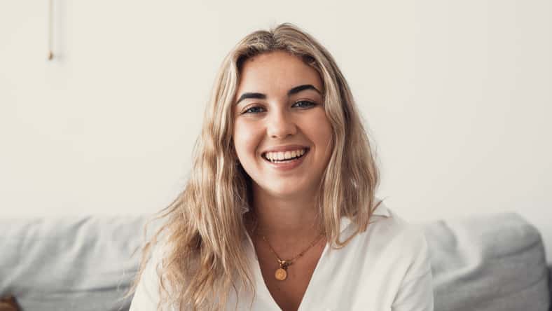 Close up overjoyed woman laughing, sitting on couch at home, head shot portrait young female chatting online with friends or relatives, looking at camera, having fun, making call or shooting video