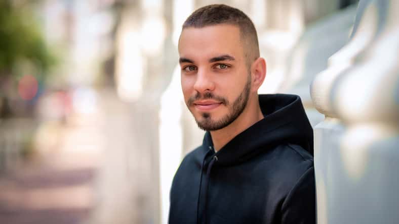 Close-up portrait of a stylish young man standing in a city street. Young male looking at camera and wearing hoodie.