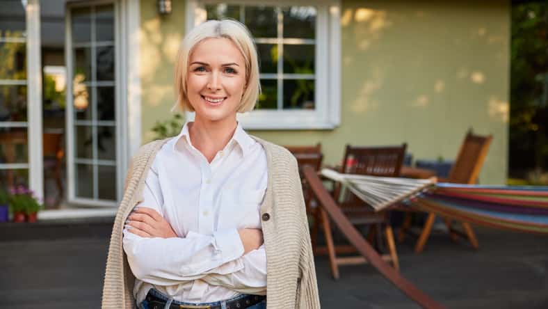 Portrait of happy mature woman standing outside her home backyard patio