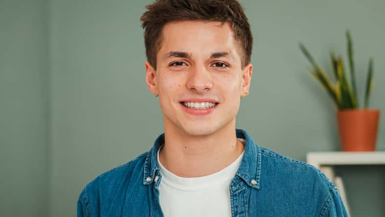 Close up individual portrait of one young adult caucasian guy smiling and looking at camera with friendly expression. Headshot of a real teenage man student with white teeth staring front at home. High quality photo