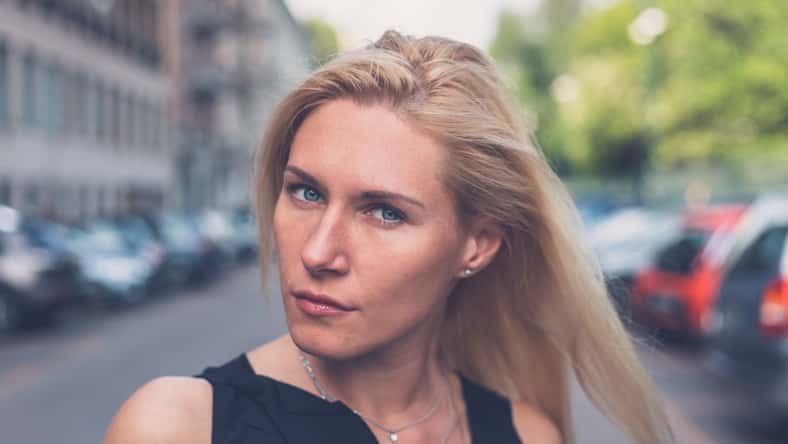 Beautiful blonde girl with black minidress and leather jacket posing in the city streets