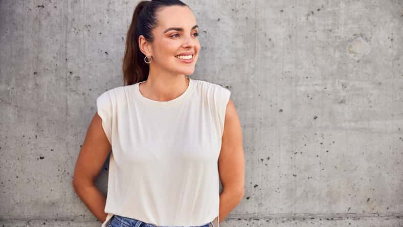 Portrait of happy mid adult woman looking away standing against concrete wall