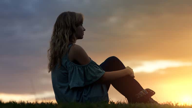 A woman sits in the grass and watches the sunset.