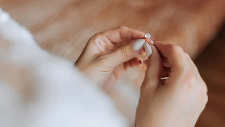 A woman is holding a ring in her hand. The ring is a diamond and it is on her finger