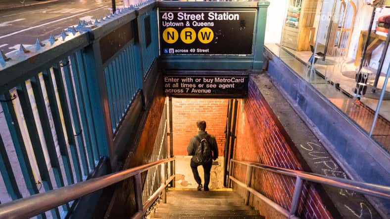 View down into lighted subway station in Manhattan at night with man on stairs