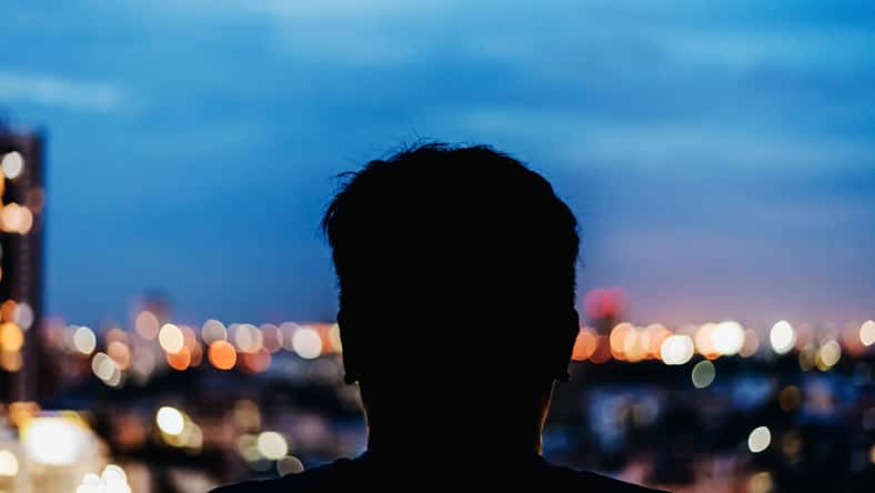 Man watching the view from skyscraper. Contours of the man to background night city. Black man silhouette in the window of a skyscraper. Dark outline man watching night city.