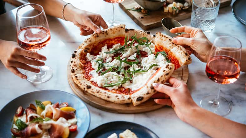 Friends enjoy a dinner party with pizza and rose wine in a bar or a restaurant.