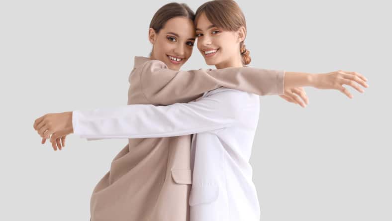 Beautiful young happy fashionable sisters in stylish outfits posing on grey background
