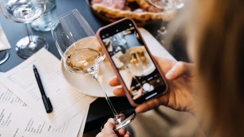 Woman photographing wine and charcuterie with smartphone