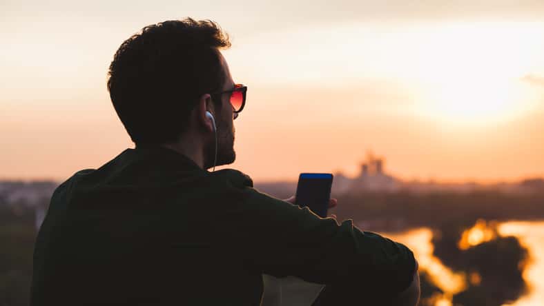 Young man enjoying sunset listening to the music on the smartphone