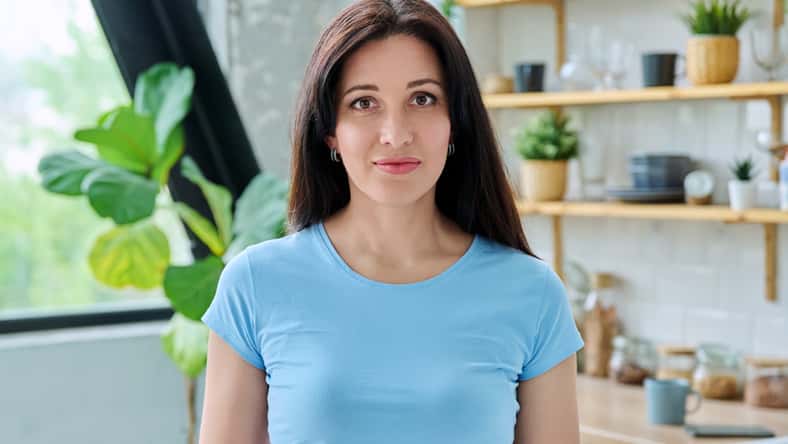 Headshot portrait young smiling woman at home in kitchen. Happy positive 30s female in blue looking at camera. Lifestyle, domestic life, people concept