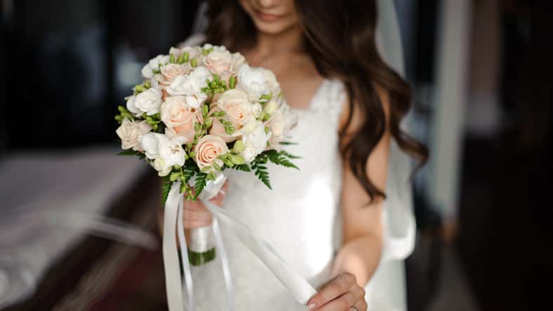 Bride morning preparation. Beautiful bride dressed in a white dress and veil holding a lovely wedding bouquet of flowers