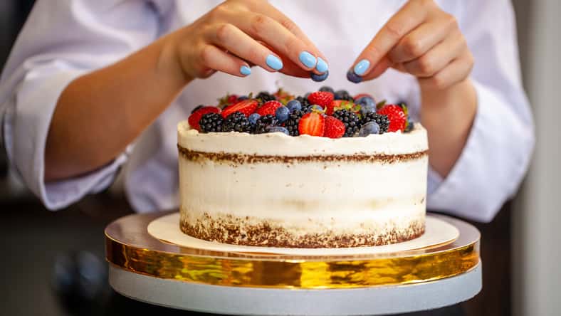 Girl chef cooks confectioner, decorates cake with forest berries. concept making without lactose cakes. Copy space, selective focus