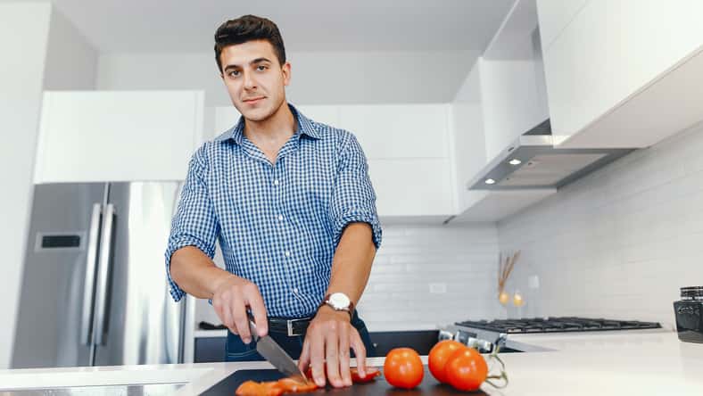 Man in a kitchen. A handsome man cut the tomatoes with a knife. Male at home with vagatables.
