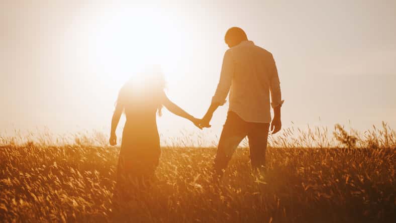 silhouettes of a couple holding hands looking at the bright sunset in a wheat field.