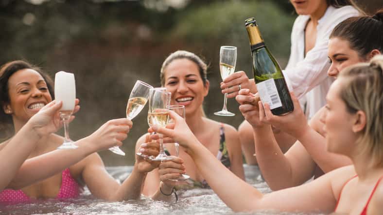 Small group of female friends socialising and relaxing in the hot tub on a weekend away. They are celebrating with a glass of champagne.