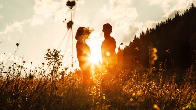 In love couple silhouets among high grass on sunset meadow