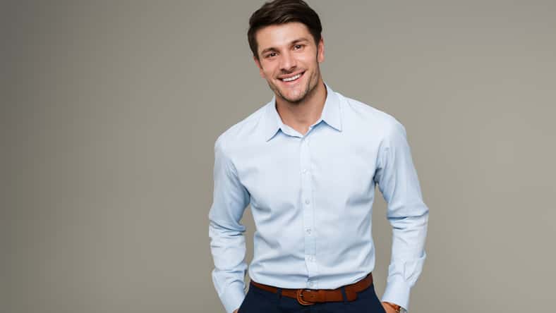 Image of happy brunette man wearing formal clothes smiling at camera with hands in pockets isolated over gray background