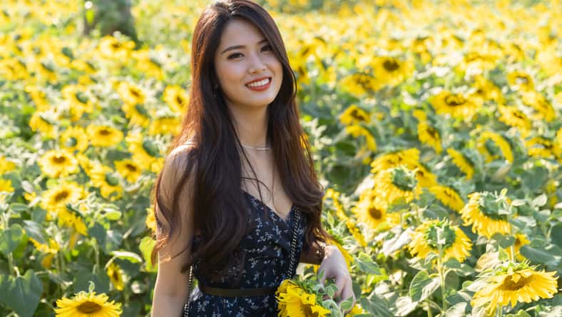 Cheerful multiracial Asian cute young woman joyful, smiling with sunflowers background. Happy carefree summer beautiful girl in sunflower field in spring.