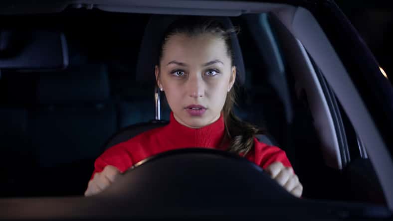 Woman is driving car at night. Serious female driver sitting inside car looks confused forward to the road clings tight to wheel on night trip. Concept: nerves and transportation. Safe journey
