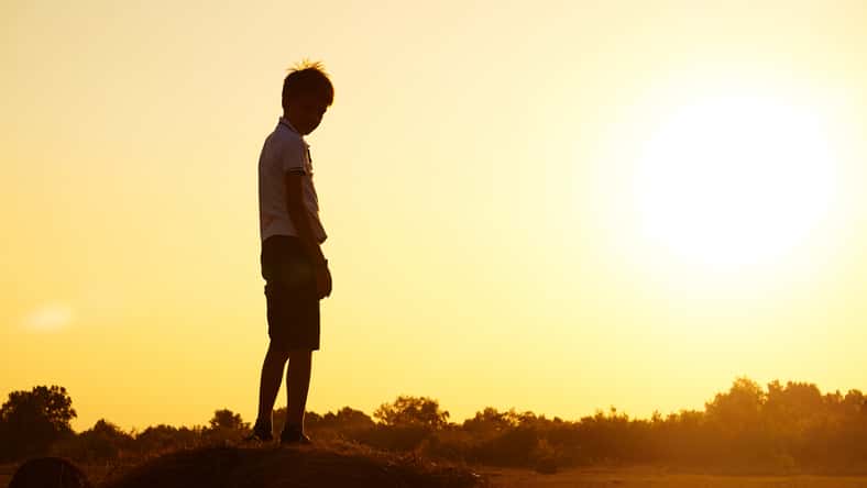 Silhouette of a child-boy standing on a haystack against the background of a field with a beautiful sunset.The concept of a carefree childhood. Beautiful summer landscape, copyspace.