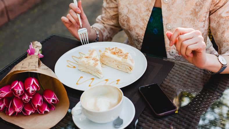 young stylish woman sitting in cafe, holding drinking cup cappuccino, eating tasty cake, tulips, happy birthday party, europe vacation, detail, close up hands, romantic dinner