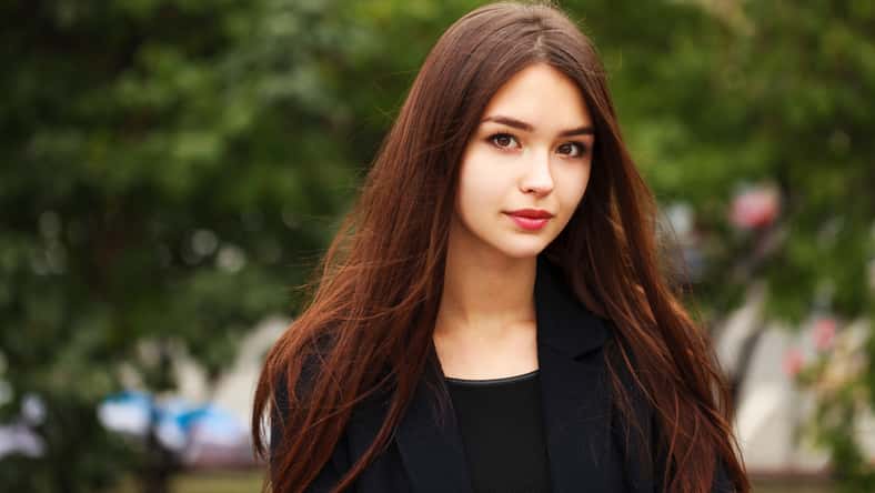 Portrait of a young girl in a dark blue autumn coat against a background of a city park