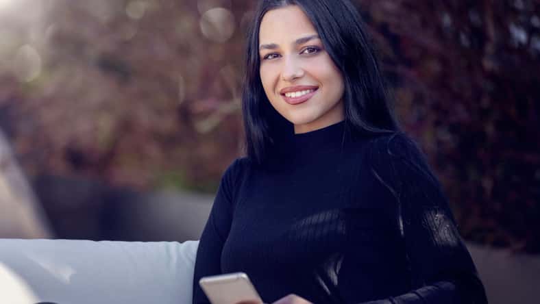 Portrait of a young woman with long black hair sitting outdoors in sunlight