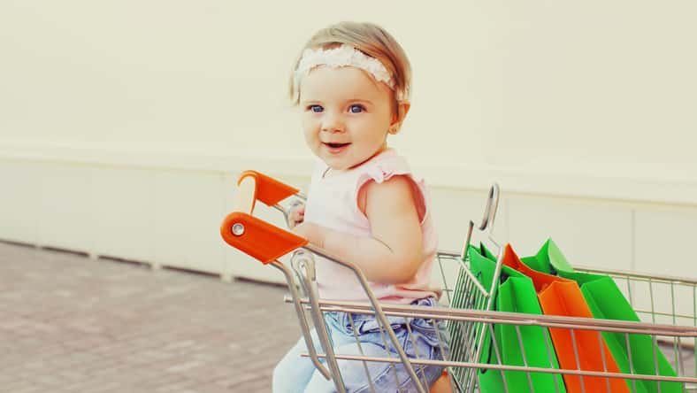 Happy baby with shopping bags sitting in a trolley cart in a city