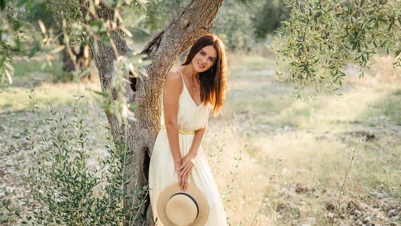 Tender portrait of beautiful brunette woman in beautiful sunlight. Woman in yellow summer linen dress in olive tree garden. Natural beauty.Travel to Italy, summer vacation. High quality photo