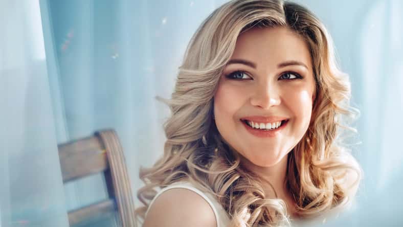 portrait of a beautiful smiling woman with blond hair on a blue background