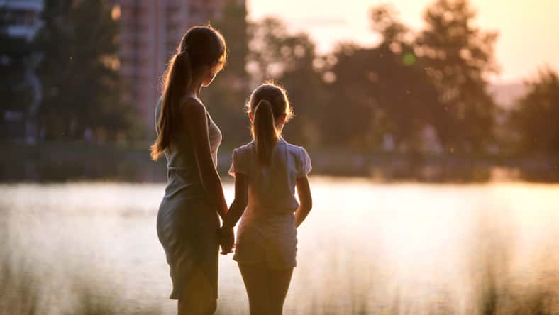 Happy mother and daughter standing together looking at building under construction dreaming about their future home at sunset. Family love and relationship concept.
